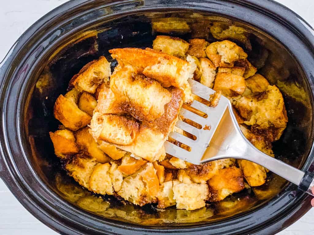Piece of crock pot french toast being lifted out of the slow cooker with a spatula.