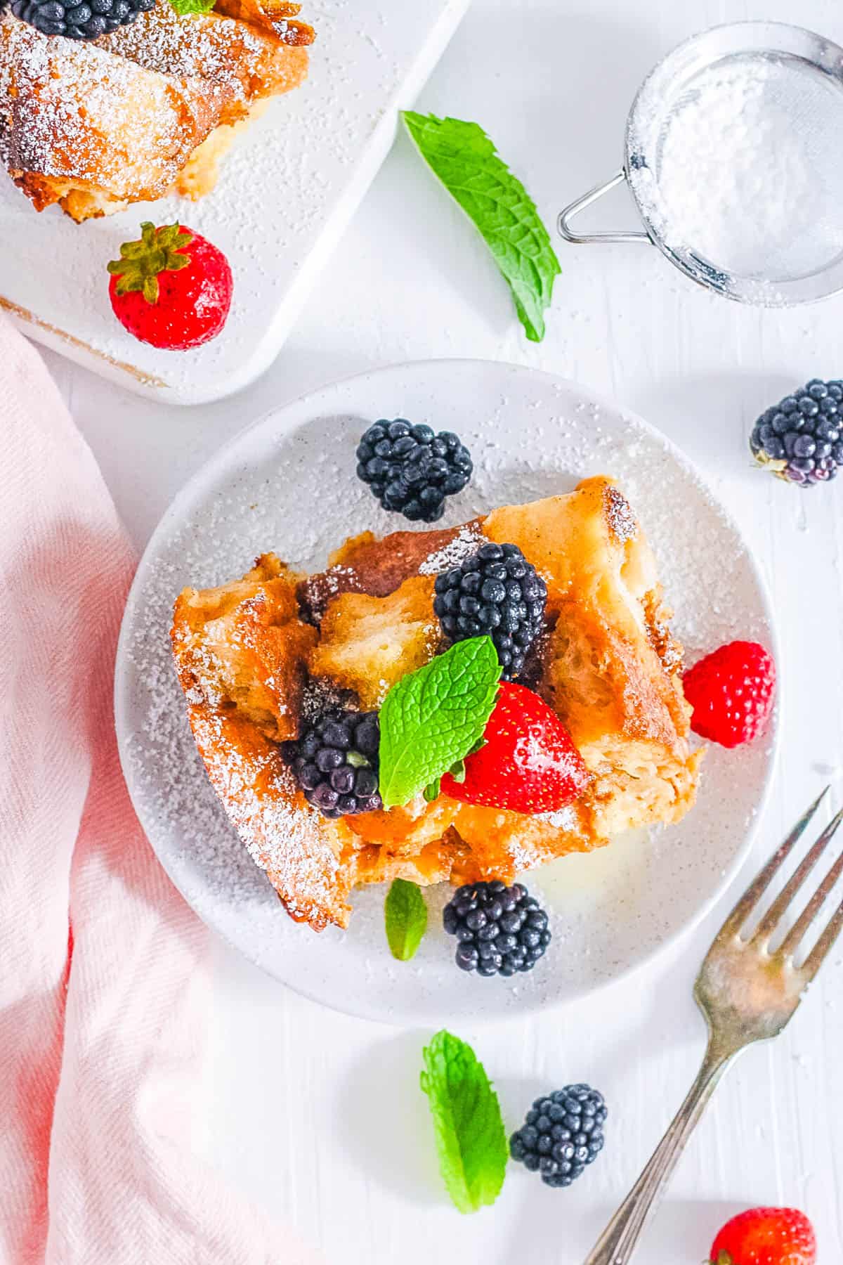 Crock pot french toast casserole topped with berries and mint, on a white plate.