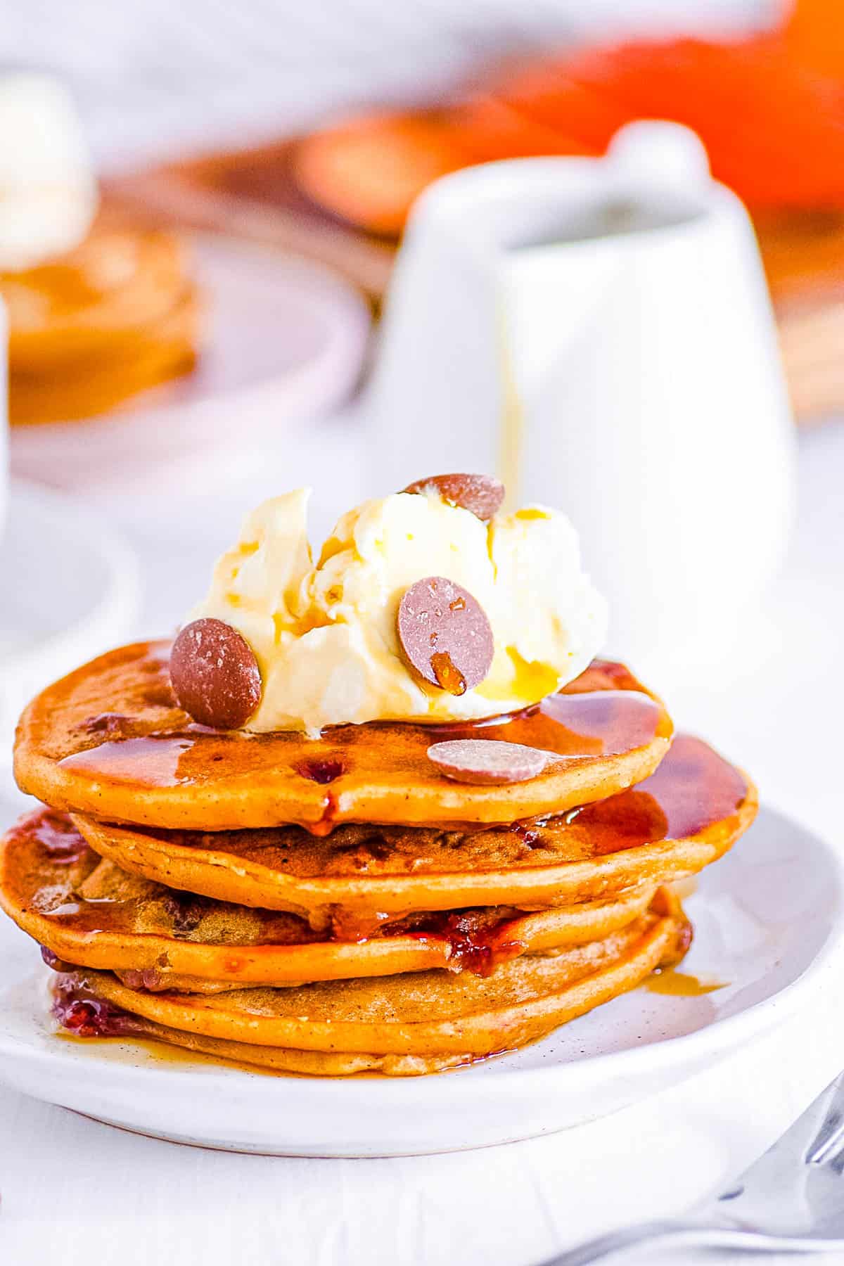 Vegan sweet potato pancakes topped with chocolate chips and vegan whipped cream on a white plate.