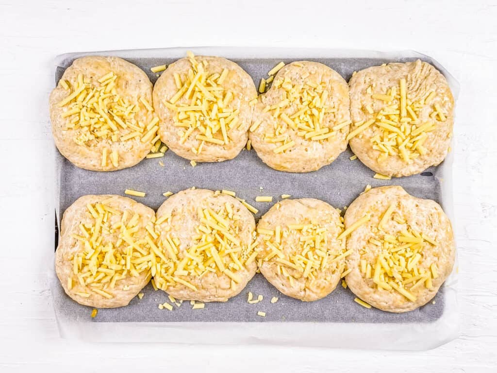 Fluffy cheese buns topped with cheddar on a baking sheet.