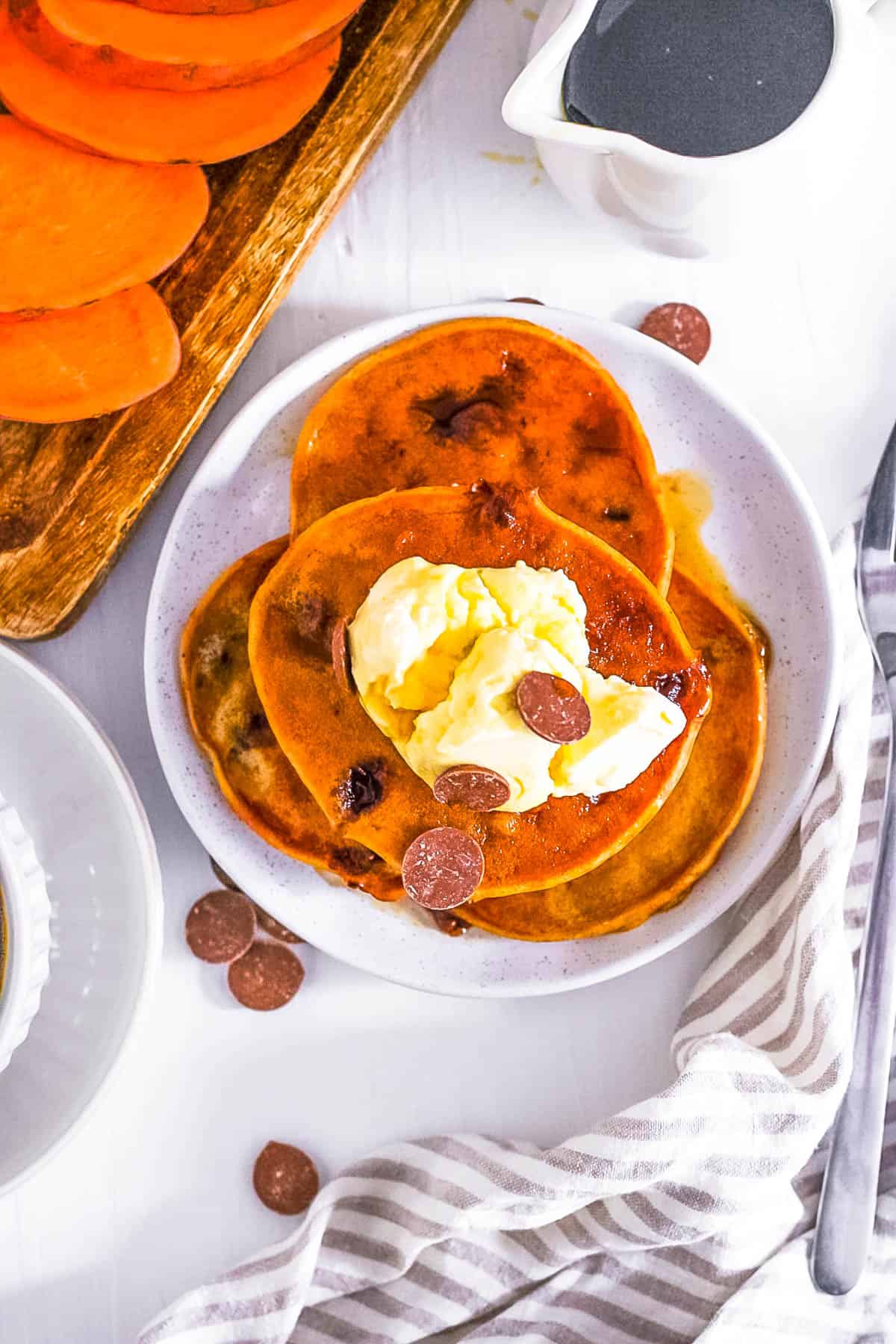 Vegan sweet potato pancakes topped with chocolate chips and vegan whipped cream on a white plate.