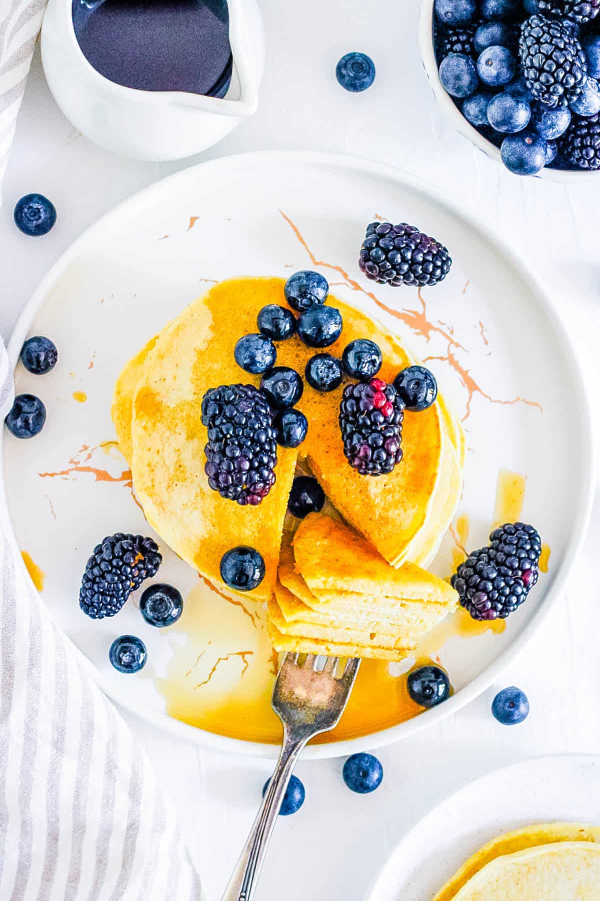 Vegan coconut flour pancakes topped with berries and syrup on a white plate.
