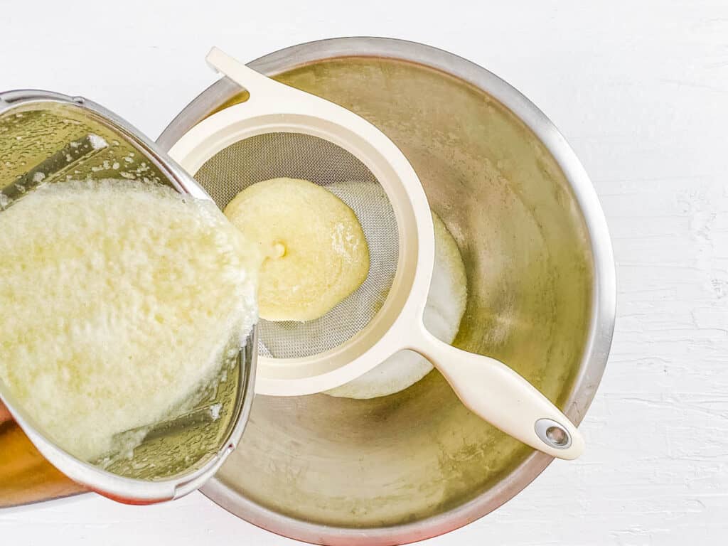 Honeydew melon puree being strained through a strainer.