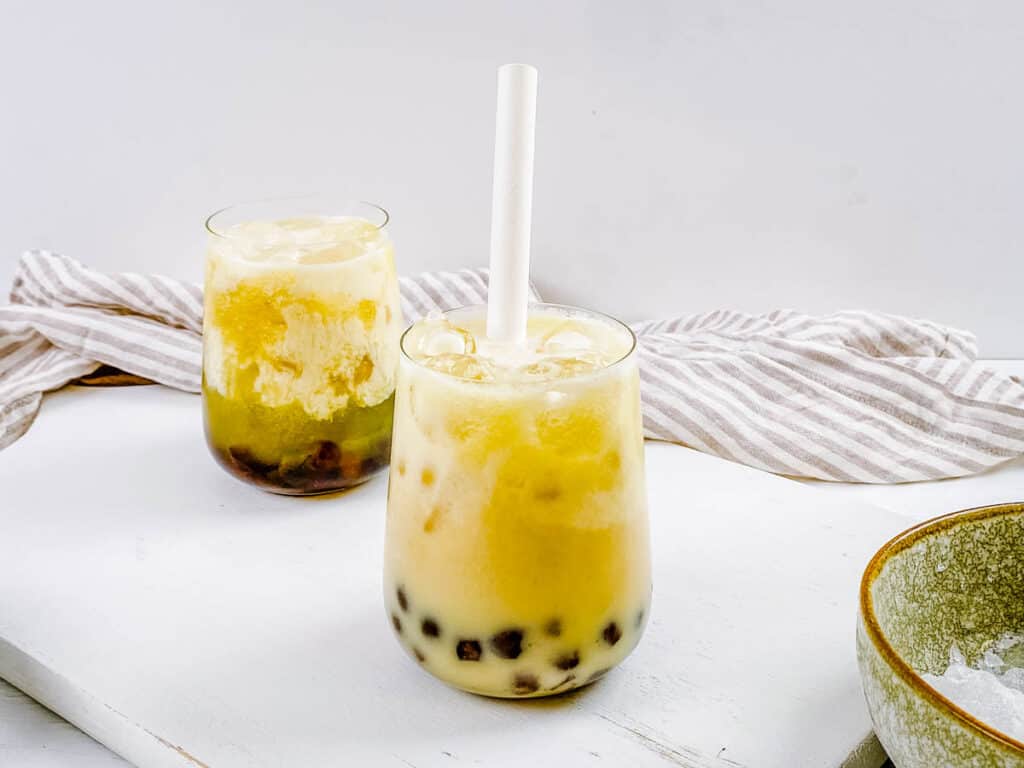 Honeydew milk tea with boba in a glass with ice and a straw.