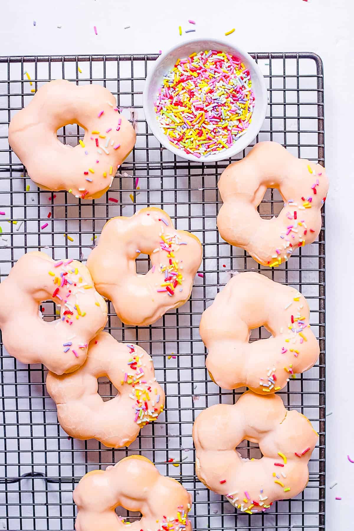 Baked mochi donuts with vegan glaze and sprinkles on a wire rack.