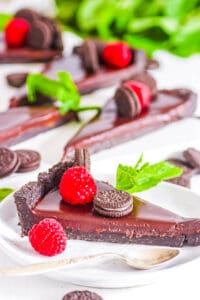 Slice of no bake chocolate Oreo tart recipe topped with berries and mini Oreo cookies on a white plate.