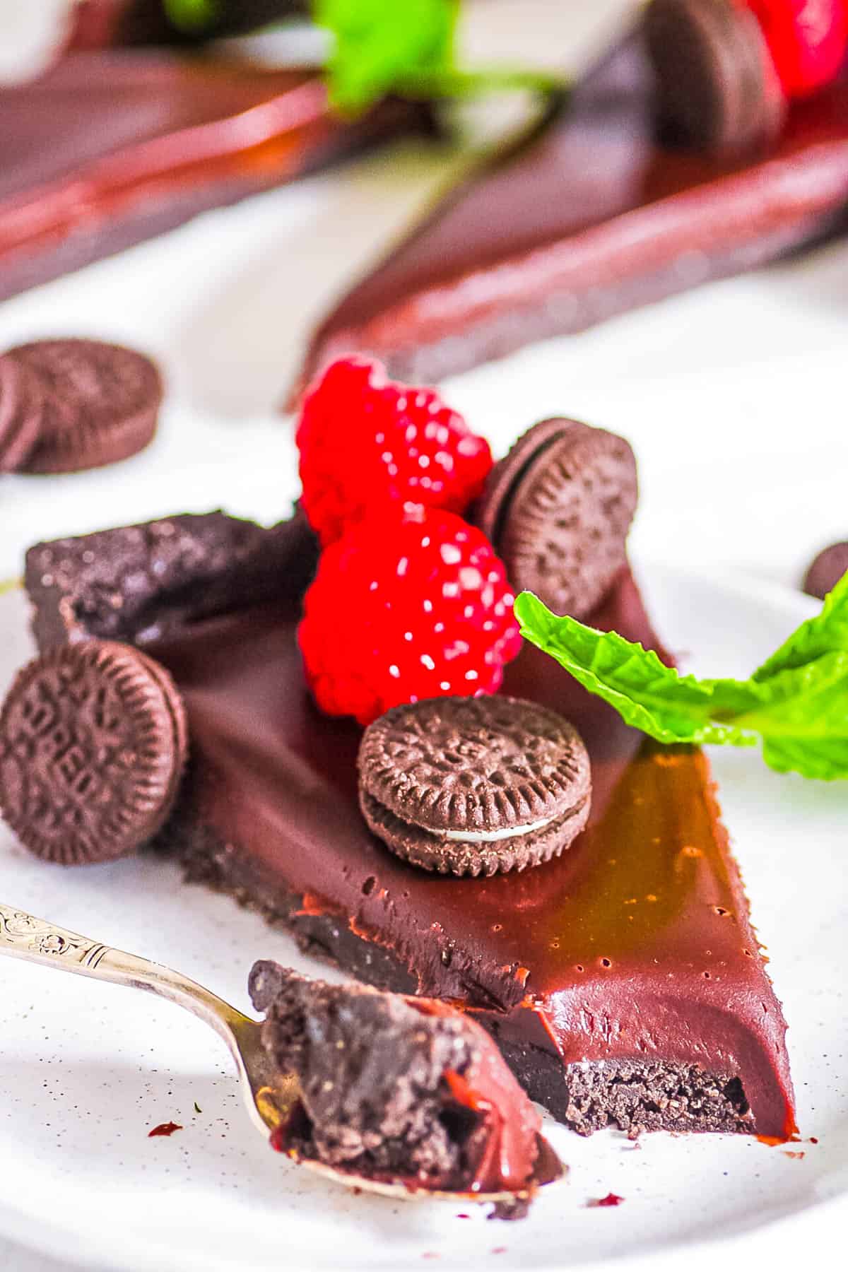 Slice of no bake chocolate Oreo tart recipe topped with berries and mini Oreo cookies on a white plate.