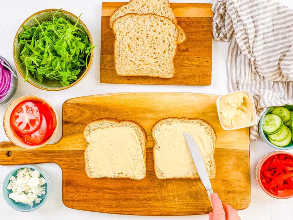 Whole wheat bread spread with hummus on a cutting board.