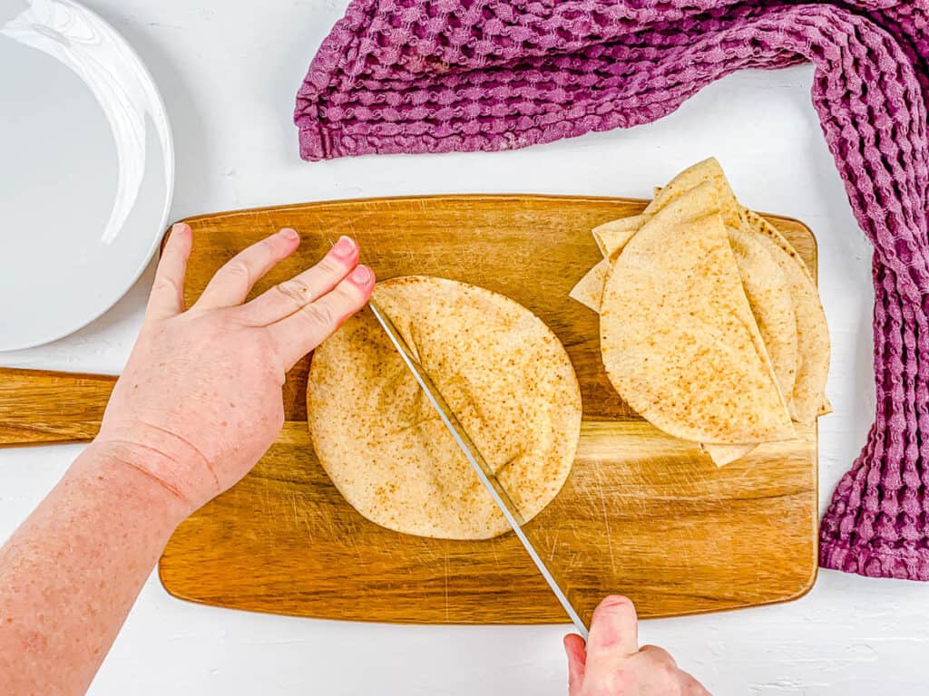 Whole wheat pita bread sliced on a cutting board.