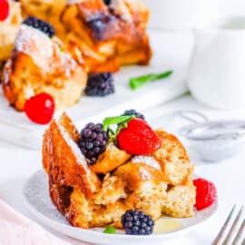 Crock pot french toast casserole topped with berries and mint, on a white plate.