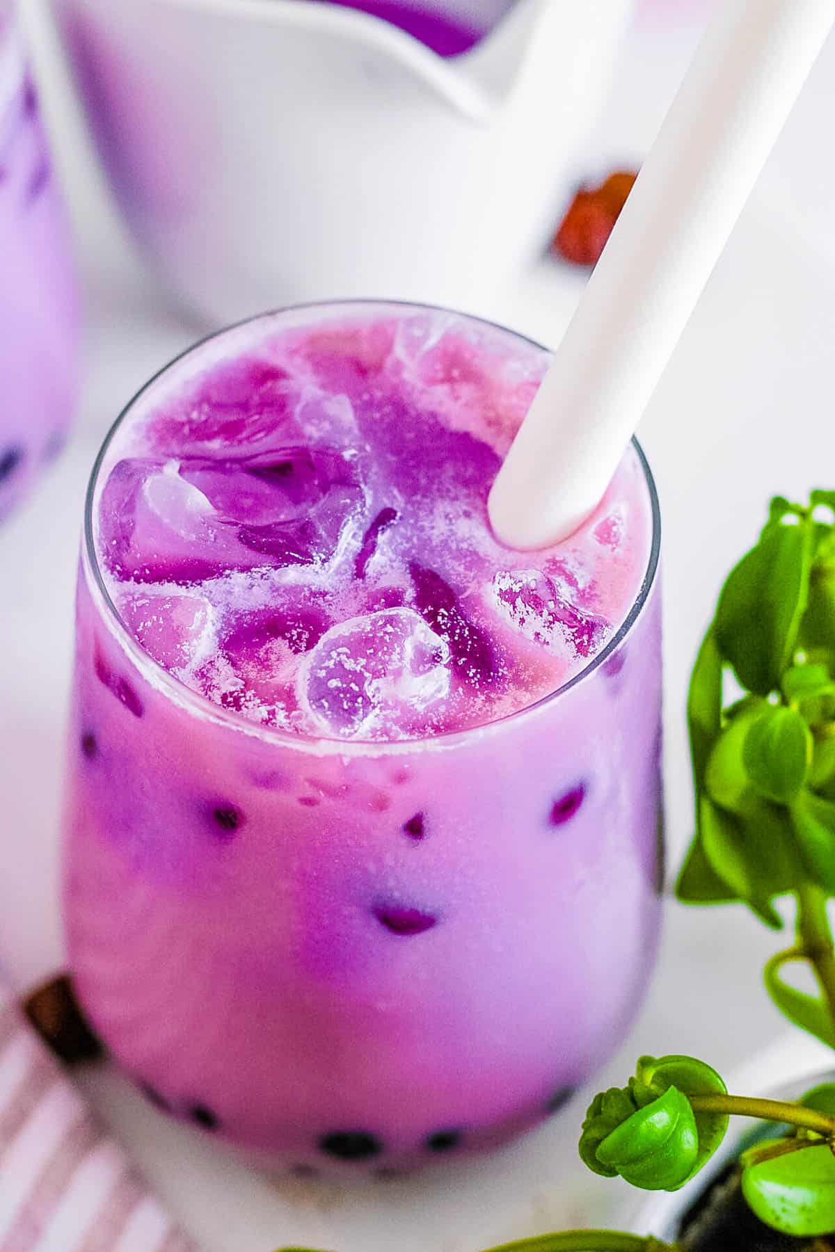 Taro bubble tea in a glass with ice and a straw.