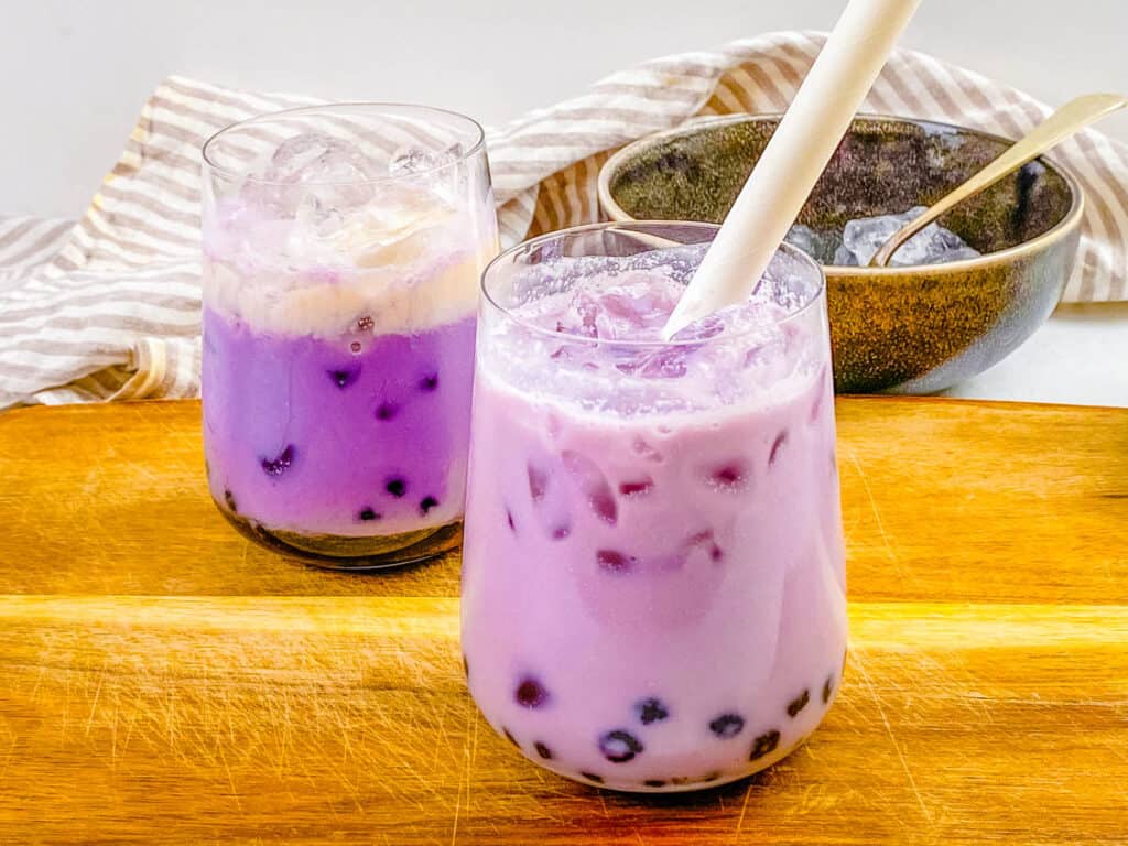 Taro milk tea with boba in a glass with a straw.