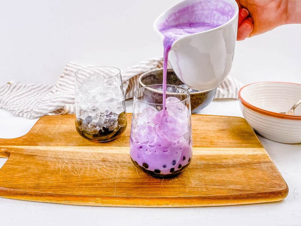Ube extract and taro milk added to purple bubble tea in a glass.
