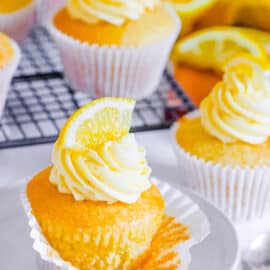 Vegan lemon cupcakes topped with vegan buttercream frosting and a lemon wedge.