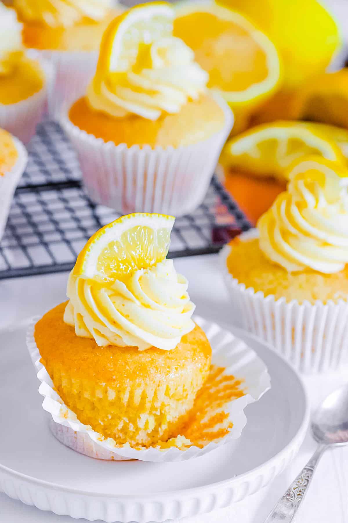 Vegan lemon cupcakes topped with vegan ،ercream frosting and a lemon wedge.
