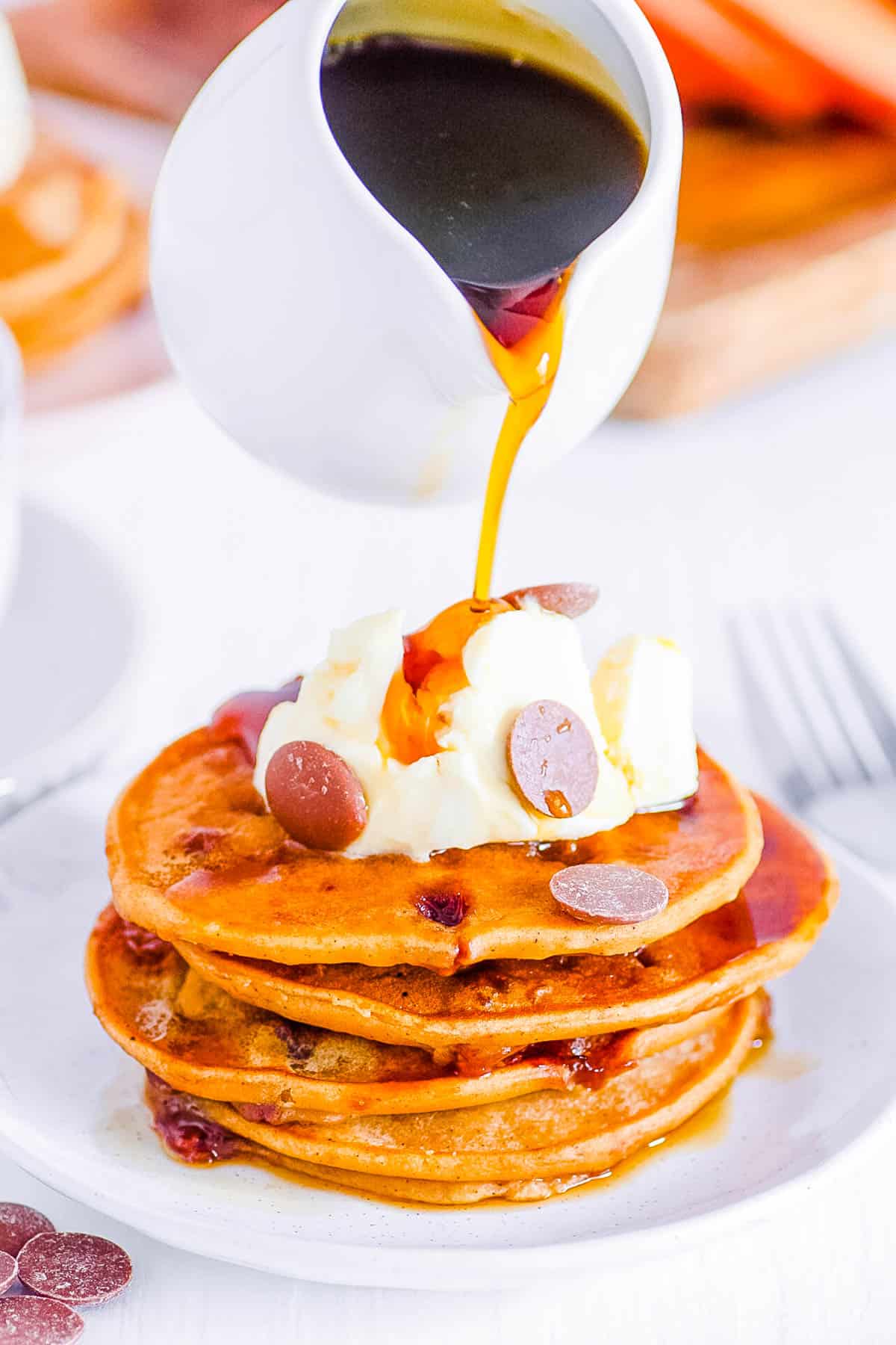 Vegan sweet potato pancakes topped with chocolate chips and vegan whipped cream on a white plate.