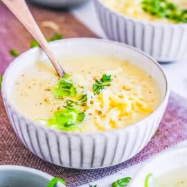 4 ingredient potato soup served in a white bowl, topped with green onions and shredded cheese.