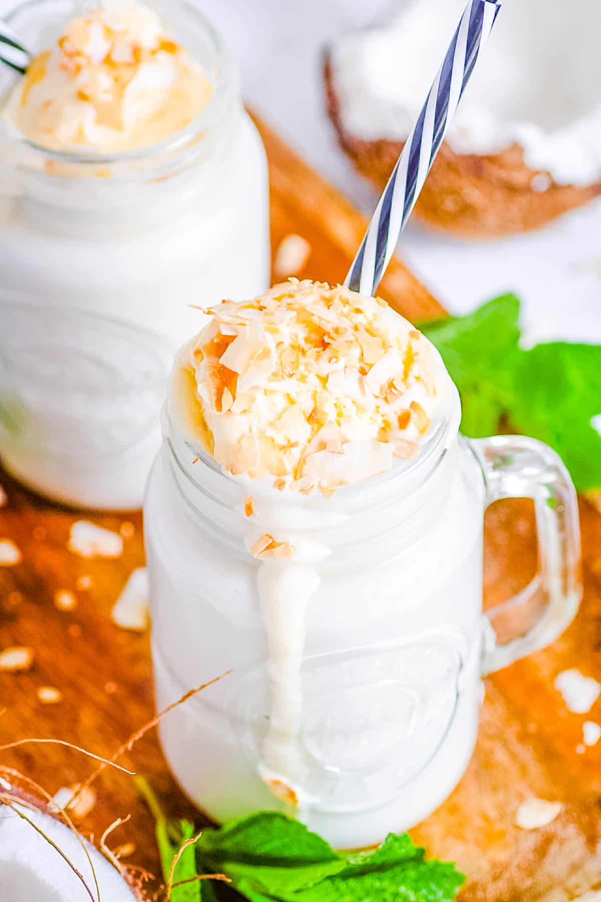 Easy coconut milkshake poured into mason jar glasses, topped with ice cream and coconut shavings.
