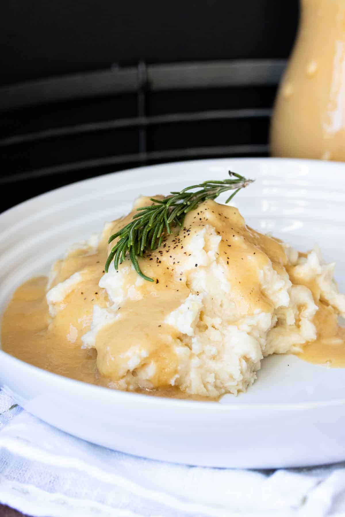 Gravy covered mashed potatoes with a sprig of rosemary on a white plate