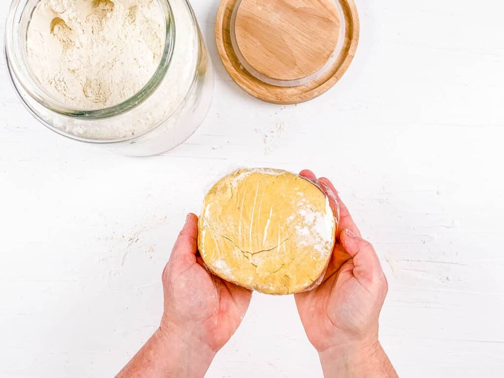 Pastry dough wrapped in plastic wrap on a white surface.