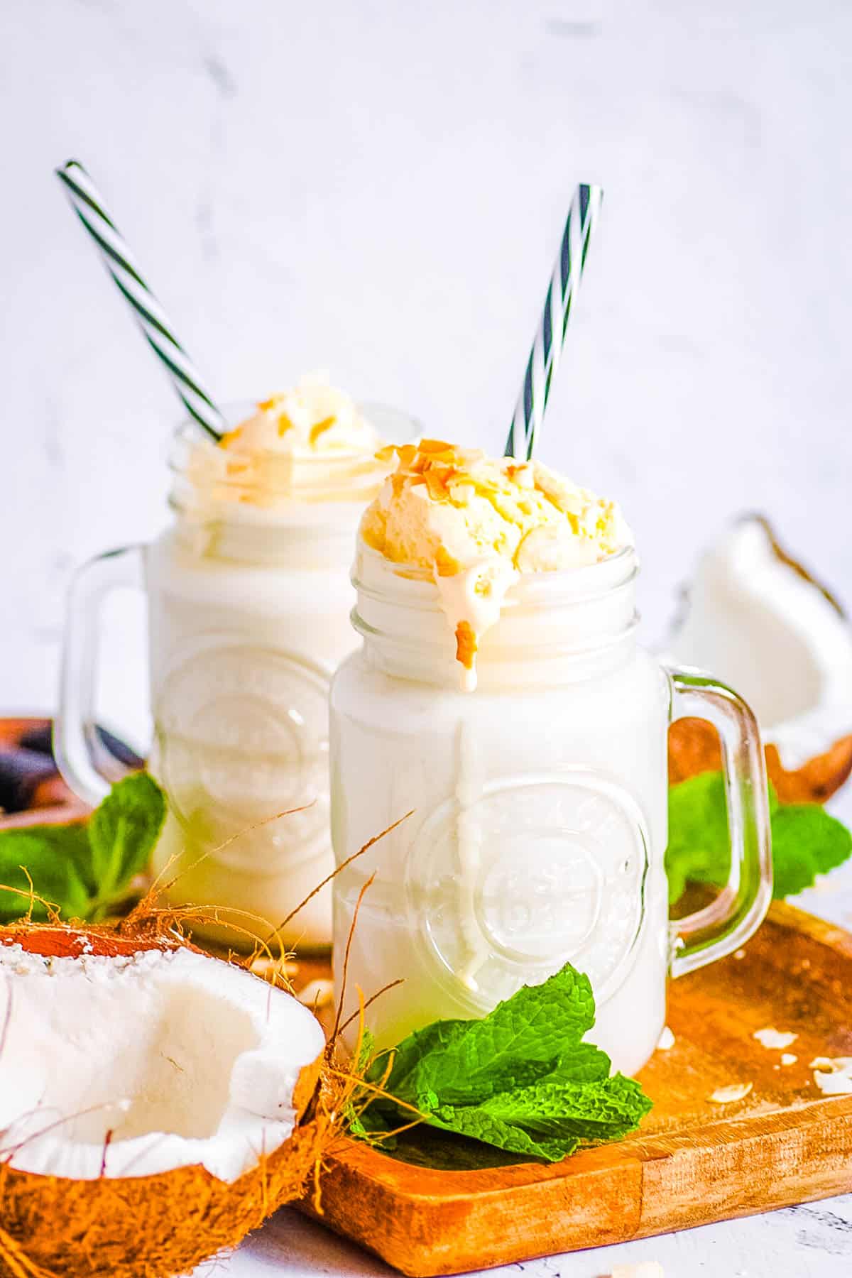 Easy coconut milkshake poured into mason jar glasses, topped with ice cream and coconut shavings.