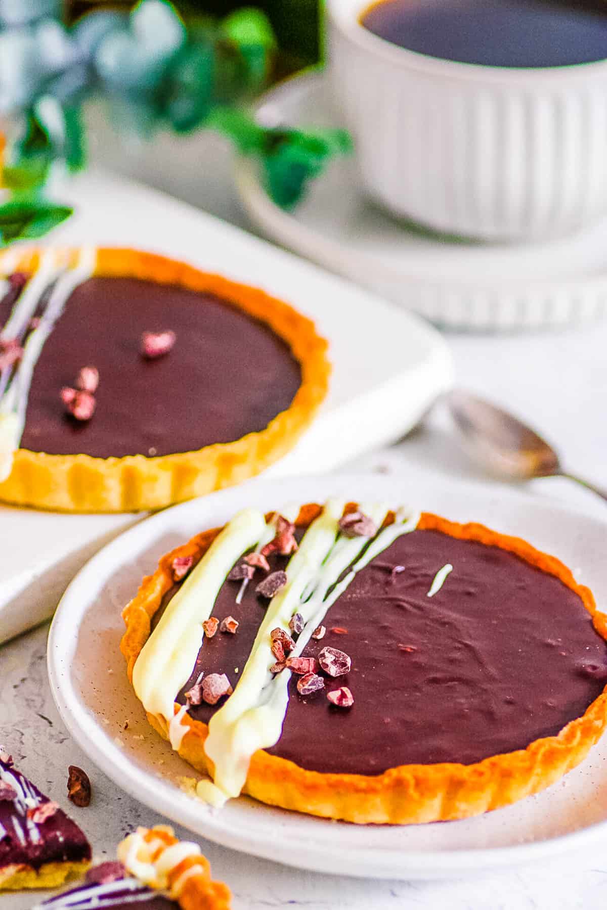 Easy mini chocolate tarts with a white chocolate drizzle on a white plate.