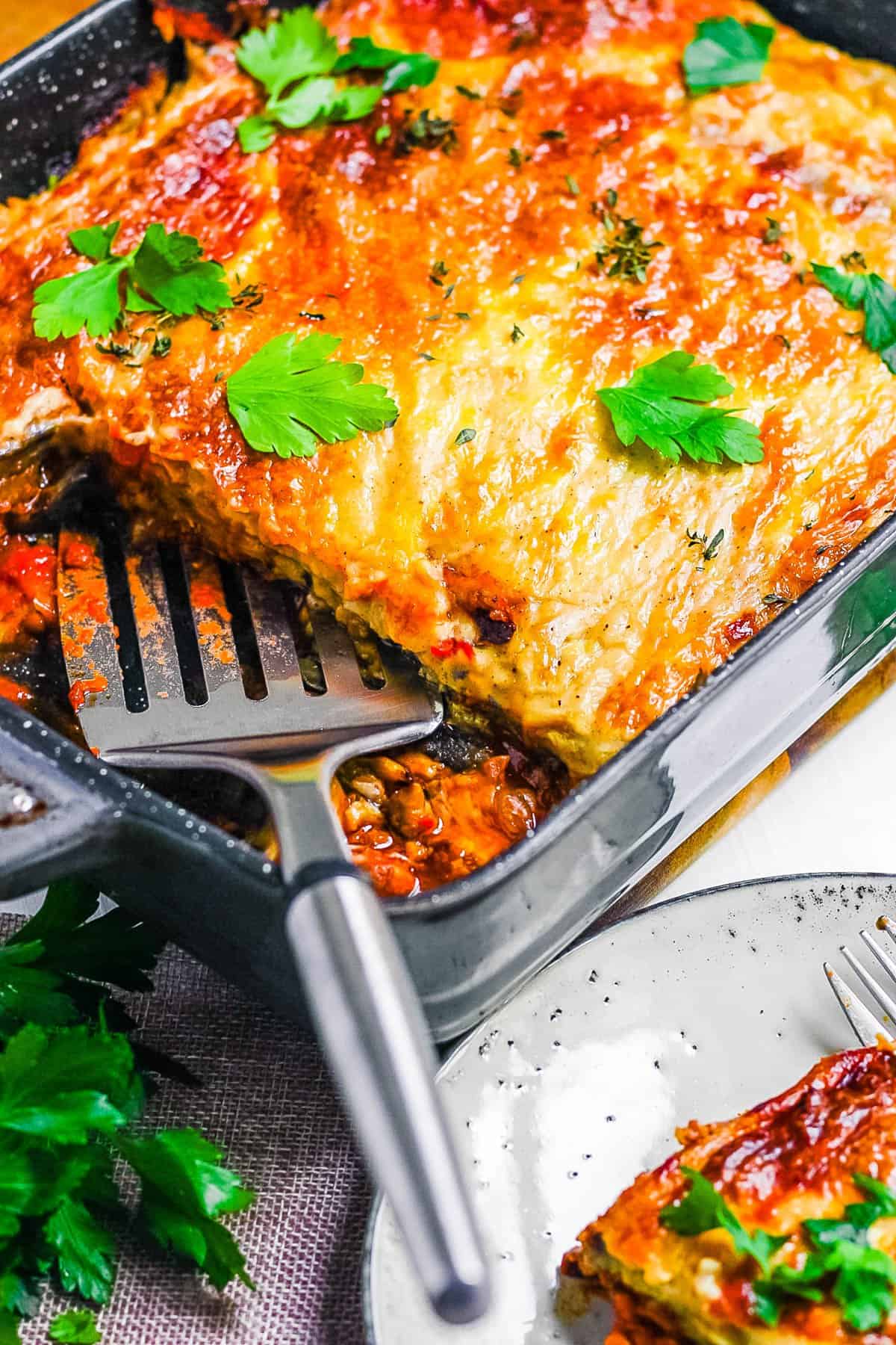 Easy vegan moussaka in a baking dish, with a slice cut out and placed on a plate.