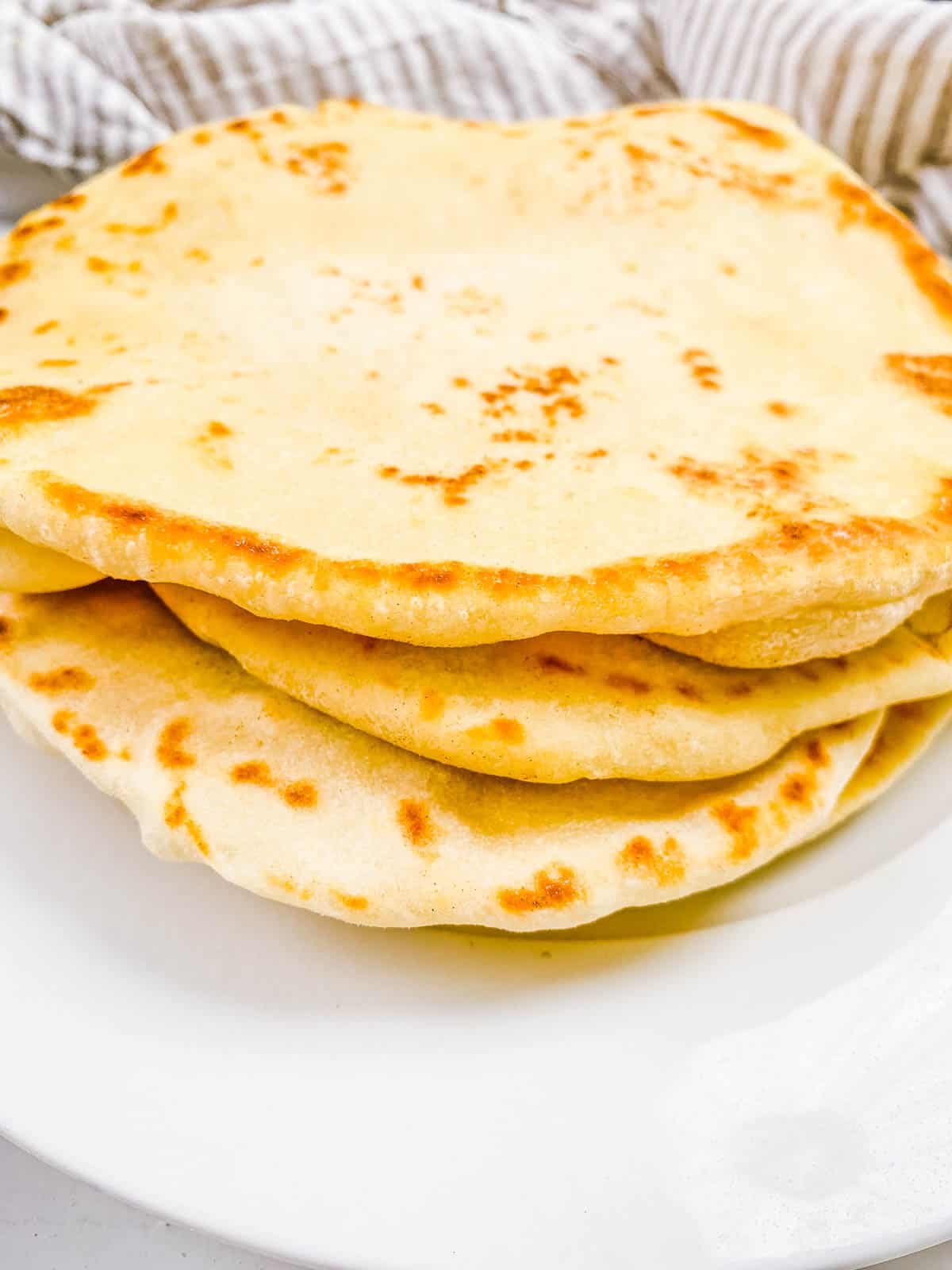 Easy vegan naan stacked on a white plate.