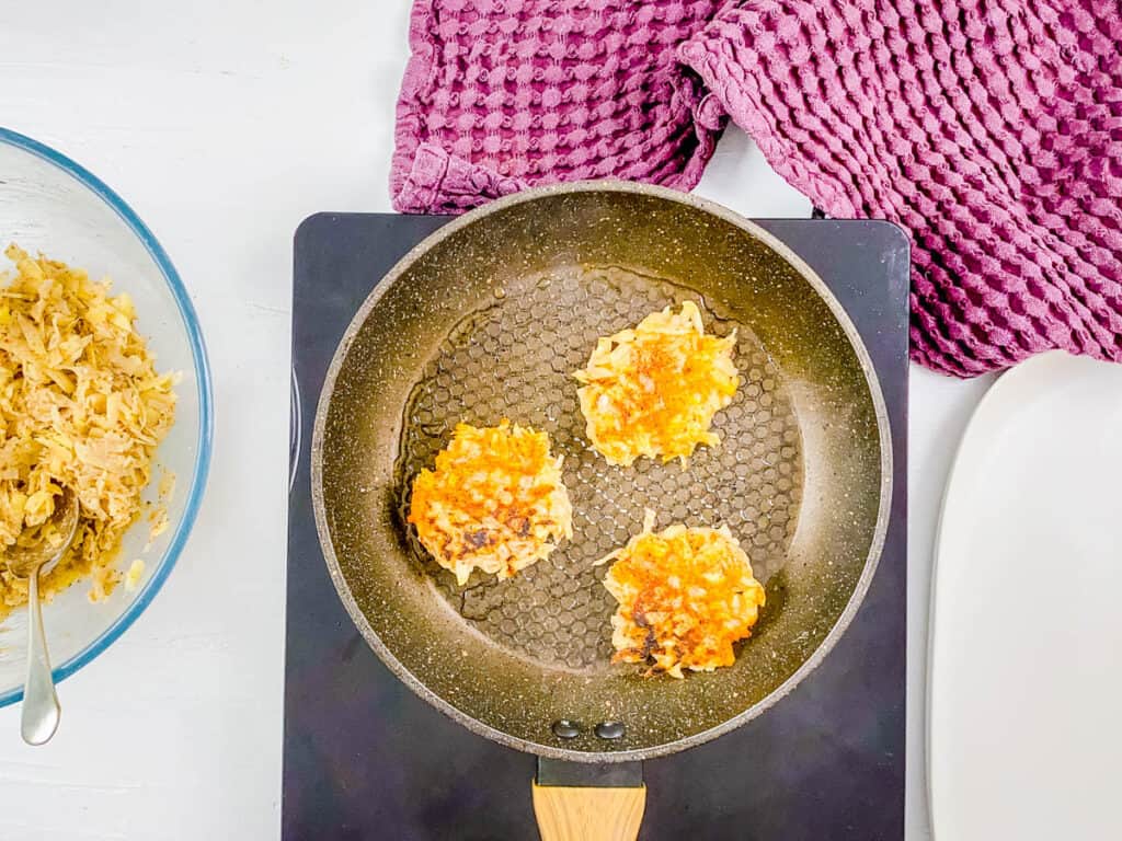 Gluten free vegan potato pancakes cooking in a nonstick skillet.