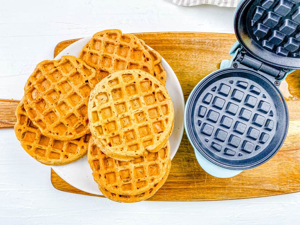 Healthy vegan protein waffles stacked on a plate next to a waffle maker.