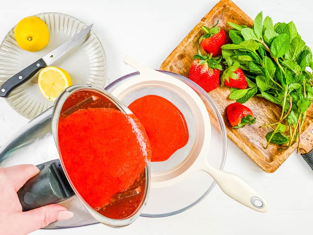 Strawberry juice strained in a strainer over a mixing bowl.