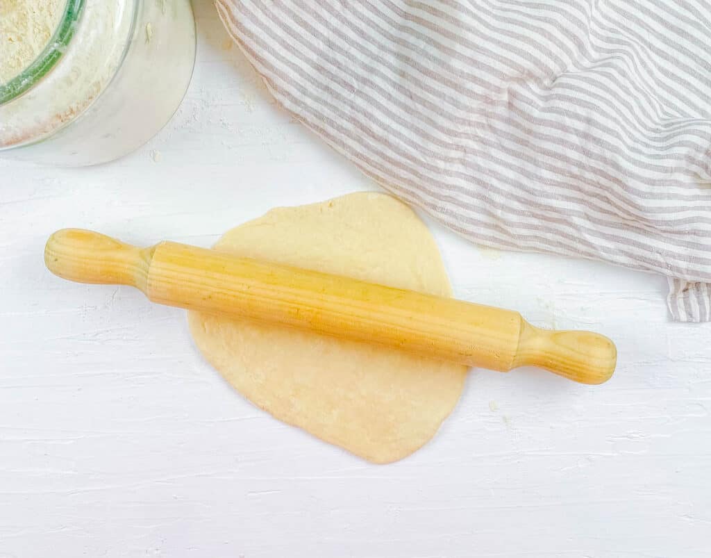 Dough for homemade vegan naan rolled out with a rolling pin.