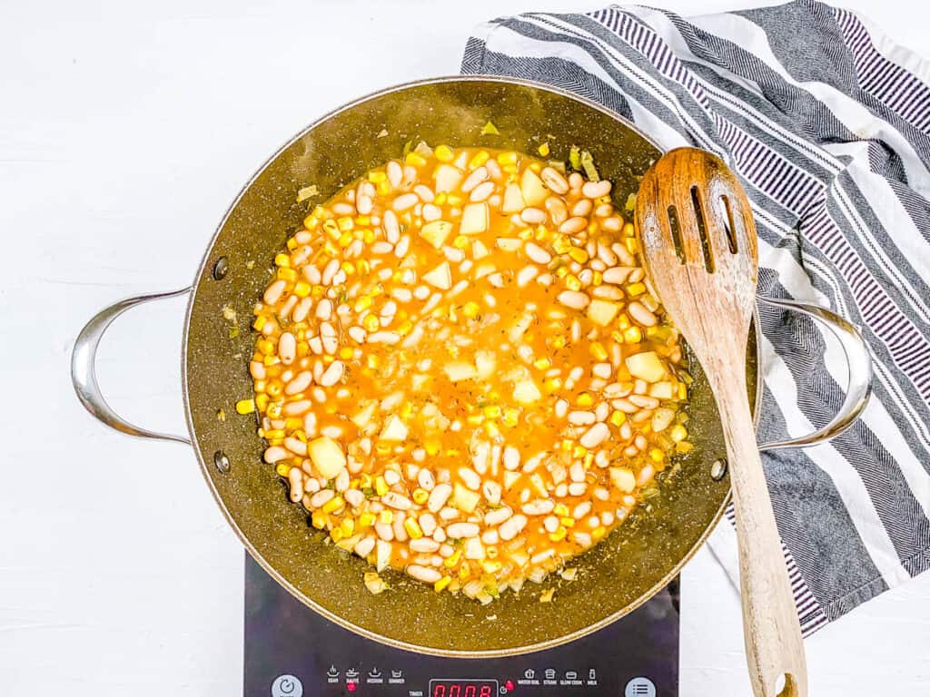 White beans and veggies cooking in vegetable broth in a pot.