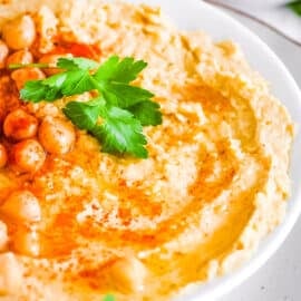 Hummus without garlic (no garlic hummus) in a white bowl garnished with parsley and paprika.