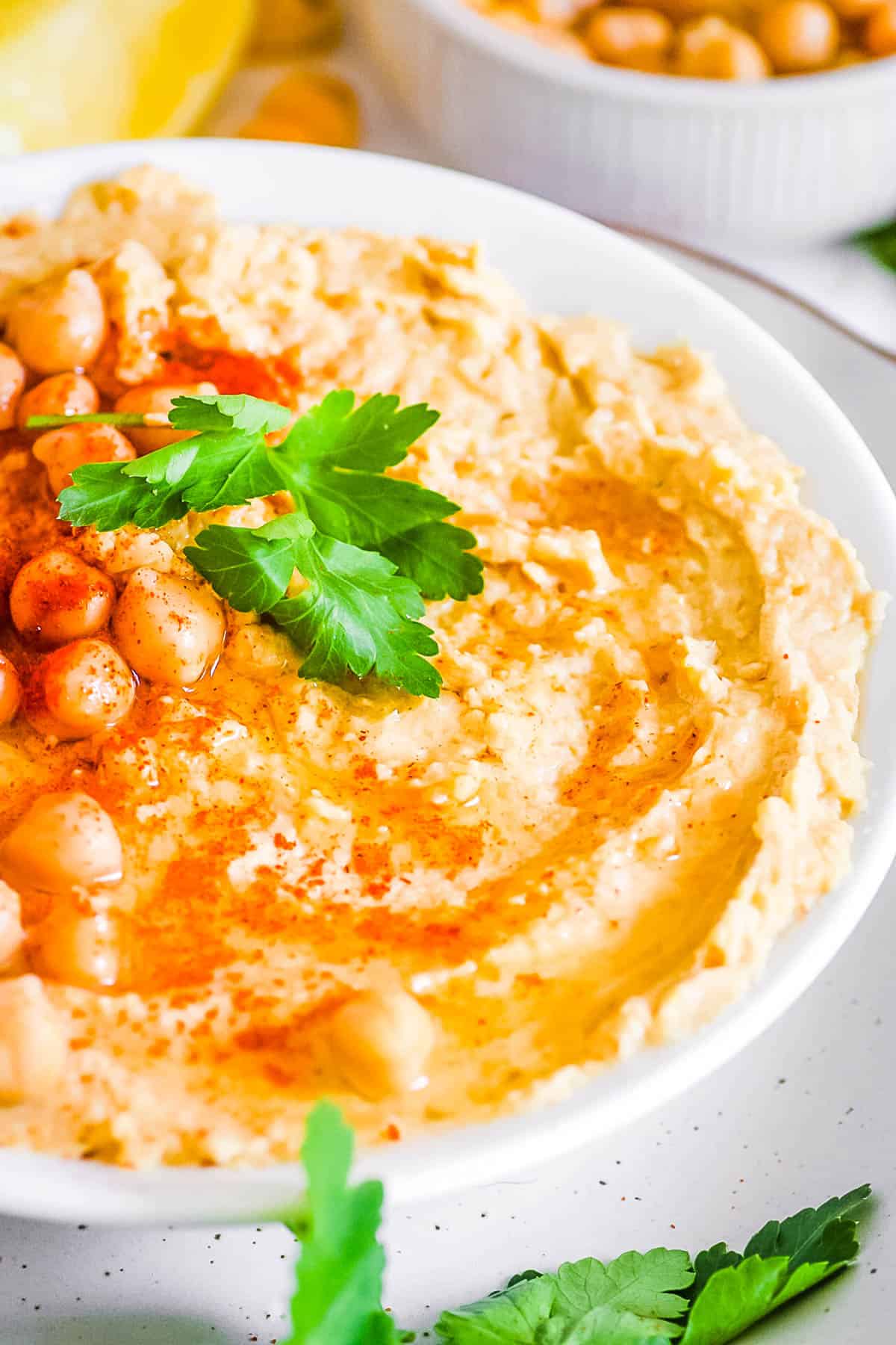 Hummus without garlic (no garlic hummus) in a white bowl garnished with parsley and paprika.