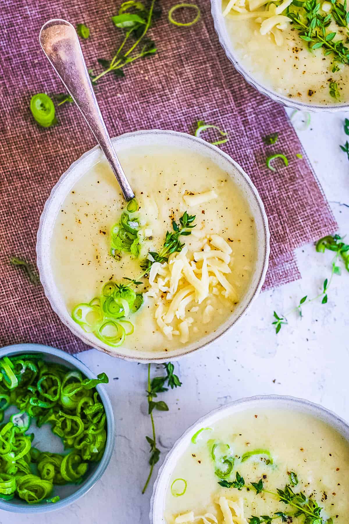 4 ingredient potato soup served in a white bowl, topped with green onions and shredded cheese.