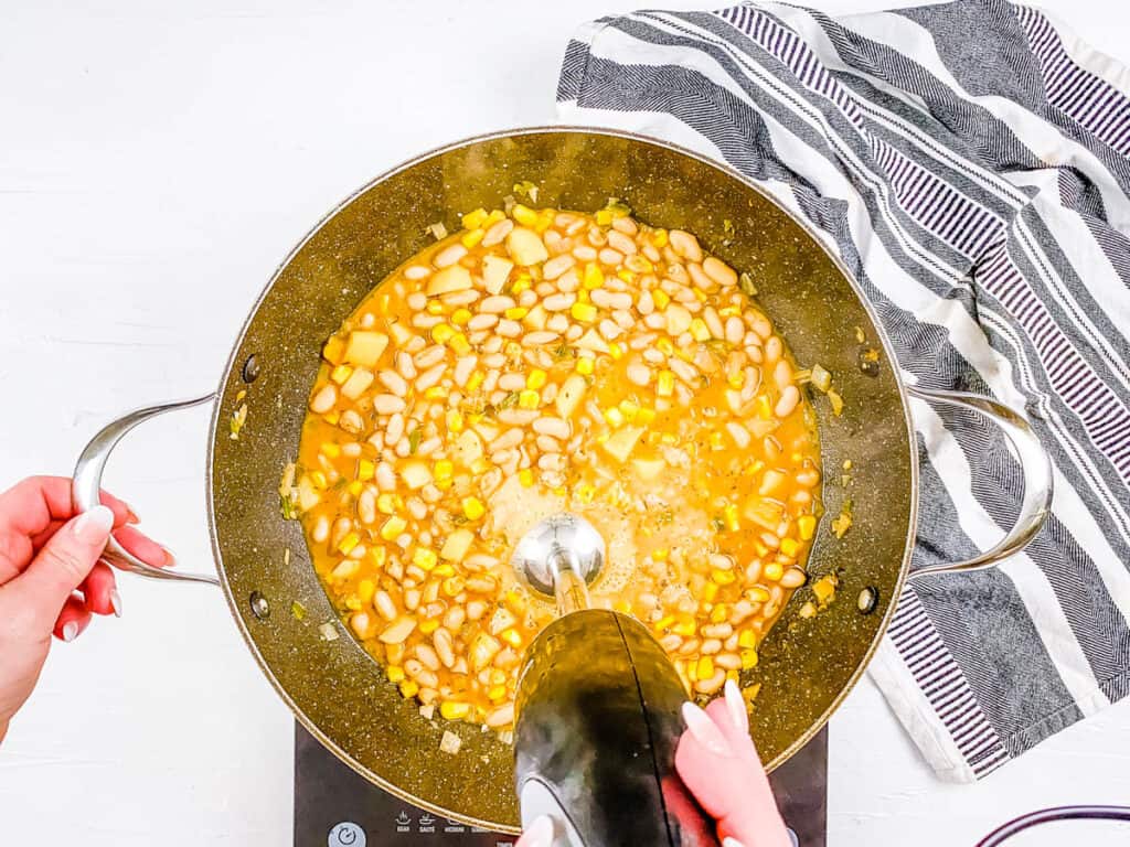 Meatless white chili being blended with an immersion blender in a stock pot.
