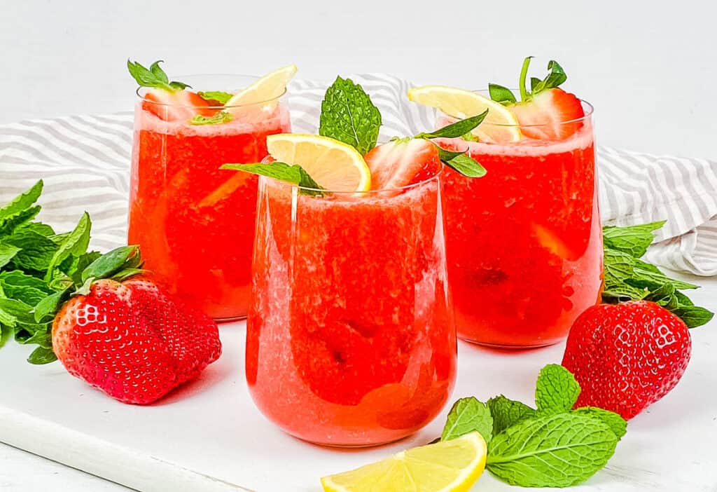 Strawberry drink in a glass garnished with mint and lemon.