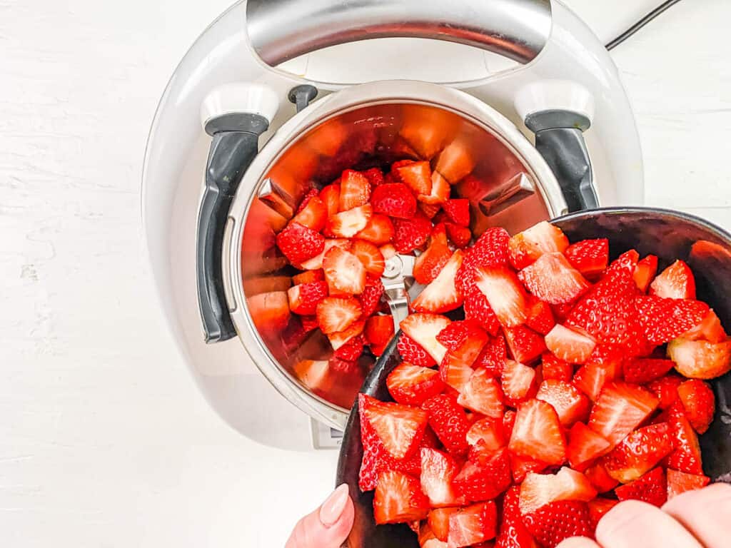 Cut strawberries being added into a blender.