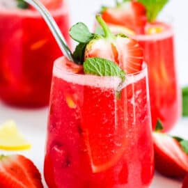 Strawberry juice in a glass with a straw, garnished with fresh strawberries and mint.