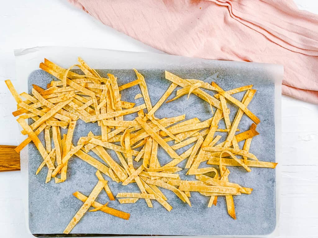 Baked corn tortilla strips on a baking sheet lined with parchment paper.