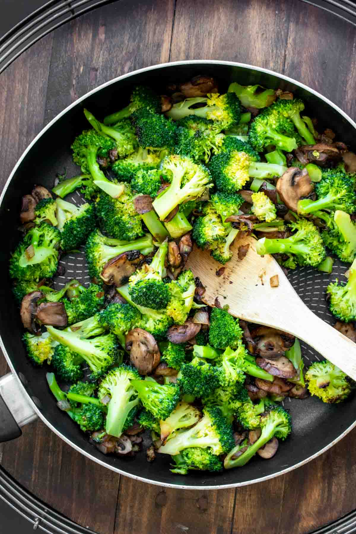 Broccoli and mushrooms sauteeing in a pan on the stove.