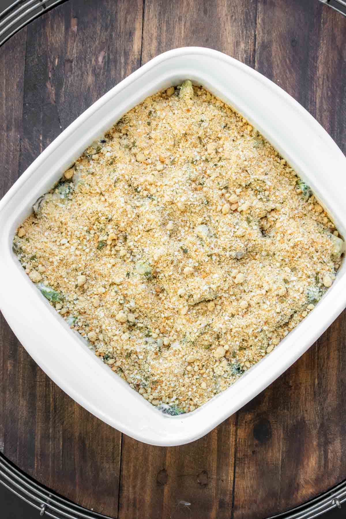 Breadcrumb topping added to vegan broccoli casserole in a white baking dish.