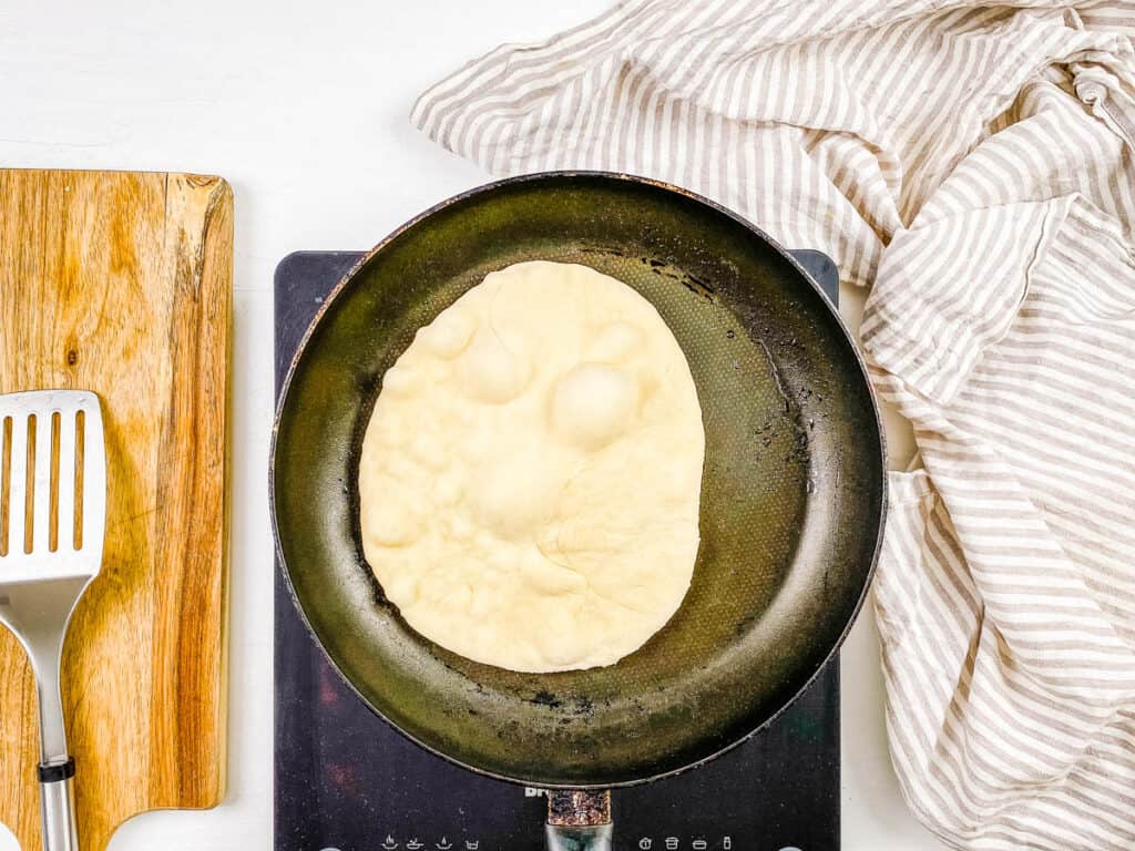 Vegan flatbread being cooked in a skillet on the stovetop.