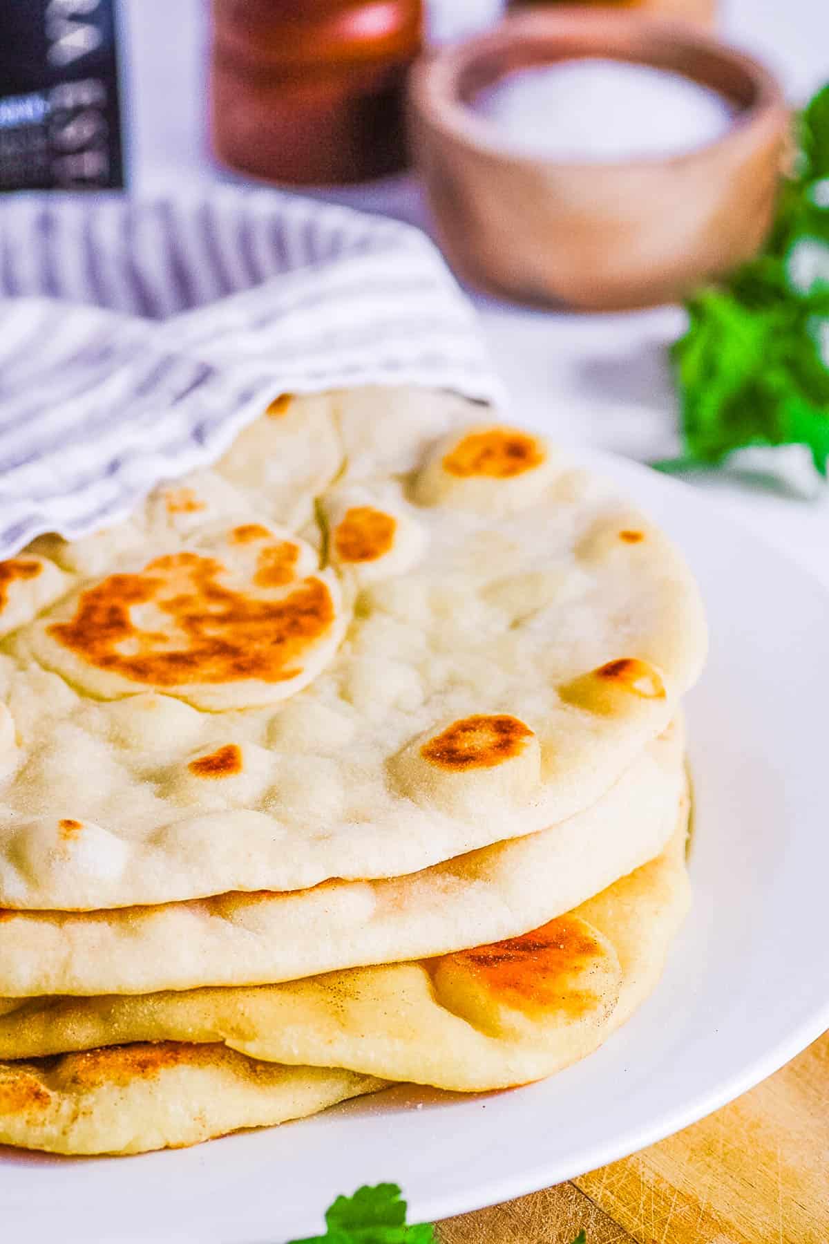 Dairy free vegan flatbread stacked on a white plate with a kitchen towel.