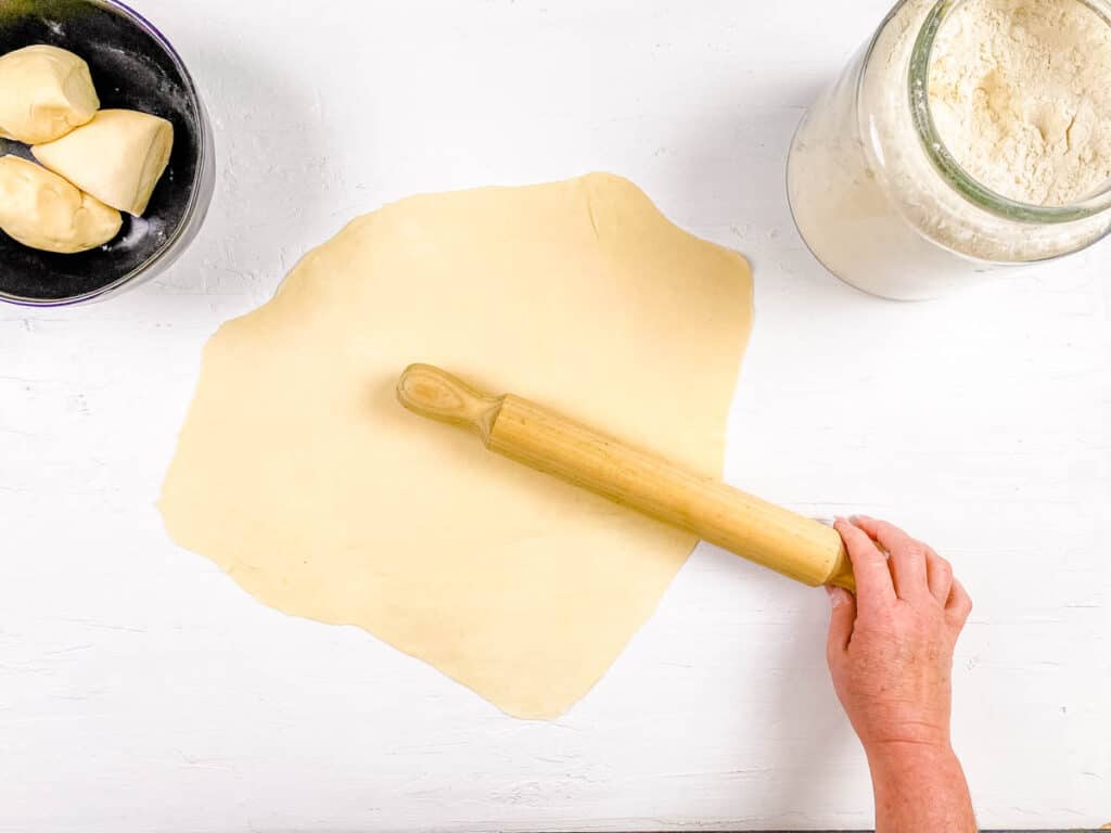 Vegan fresh pasta rolled out with a rolling pin on a cutting board.