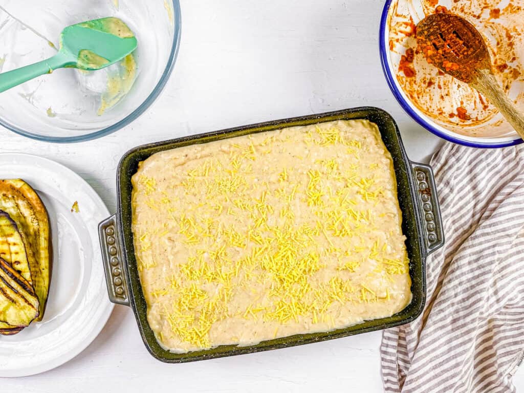 Vegan bechamel added to vegan Greek moussaka in a baking dish.