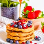 Vegan protein waffles stacked on a white plate, topped with fresh berries and maple syrup.