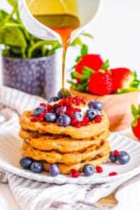 Vegan protein waffles stacked on a white plate, topped with fresh berries and maple syrup.