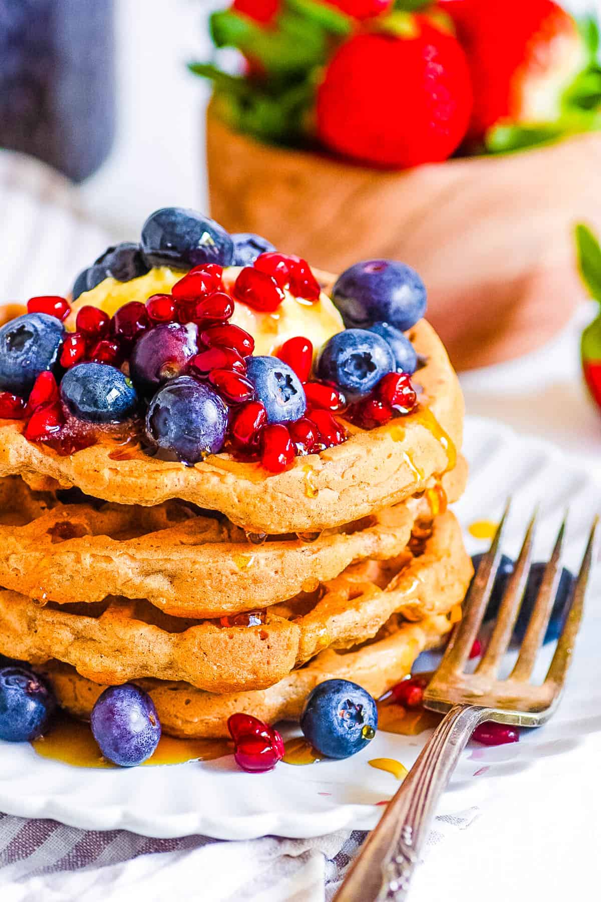 Vegan protein waffles stacked on a white plate, topped with fresh berries.